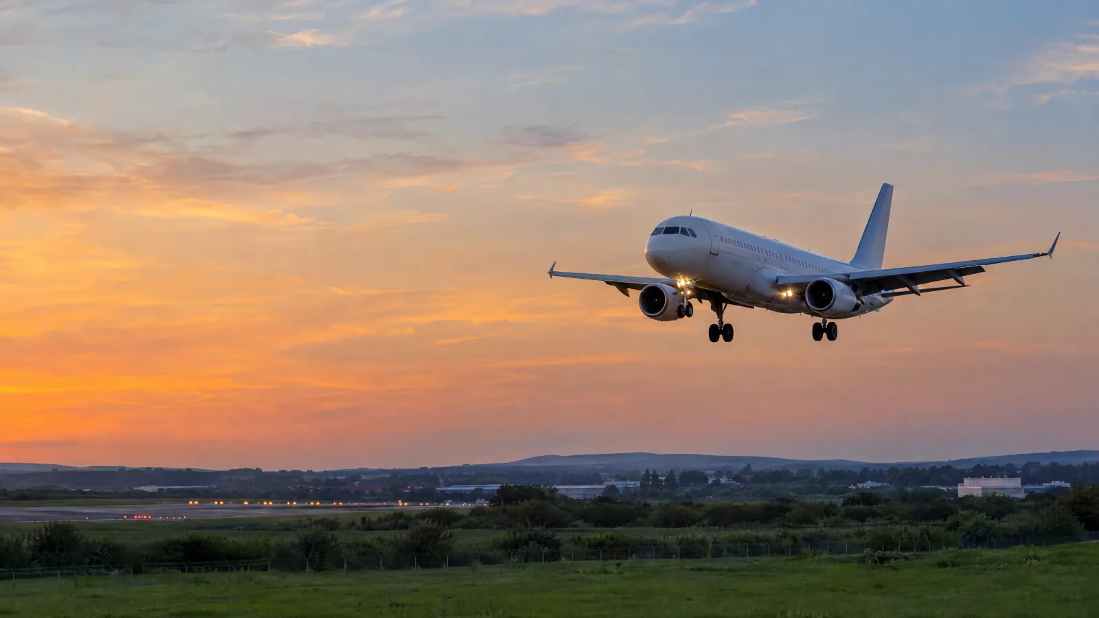 A white airliner on final approach at dusk with its landing lights on